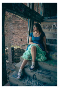 Woman in poofy dress sitting on graffiti-sprayed concrete steps next to a demolished window