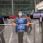 A man in an airport holding two signs - one for Neil Clarke and one for Marie Vibbert.