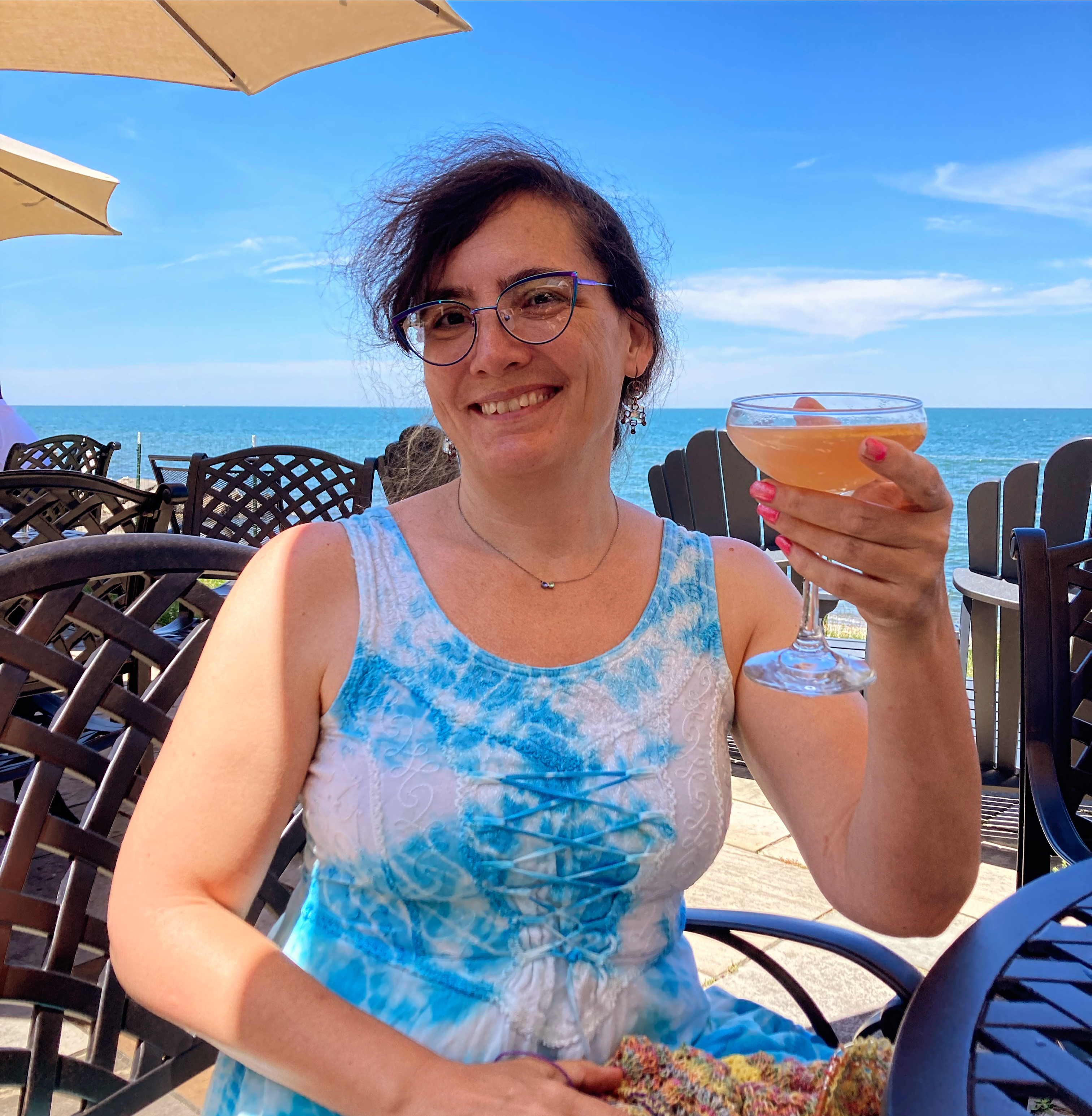 Marie holds up a cocktail with lake erie behind her on a bright sunny day