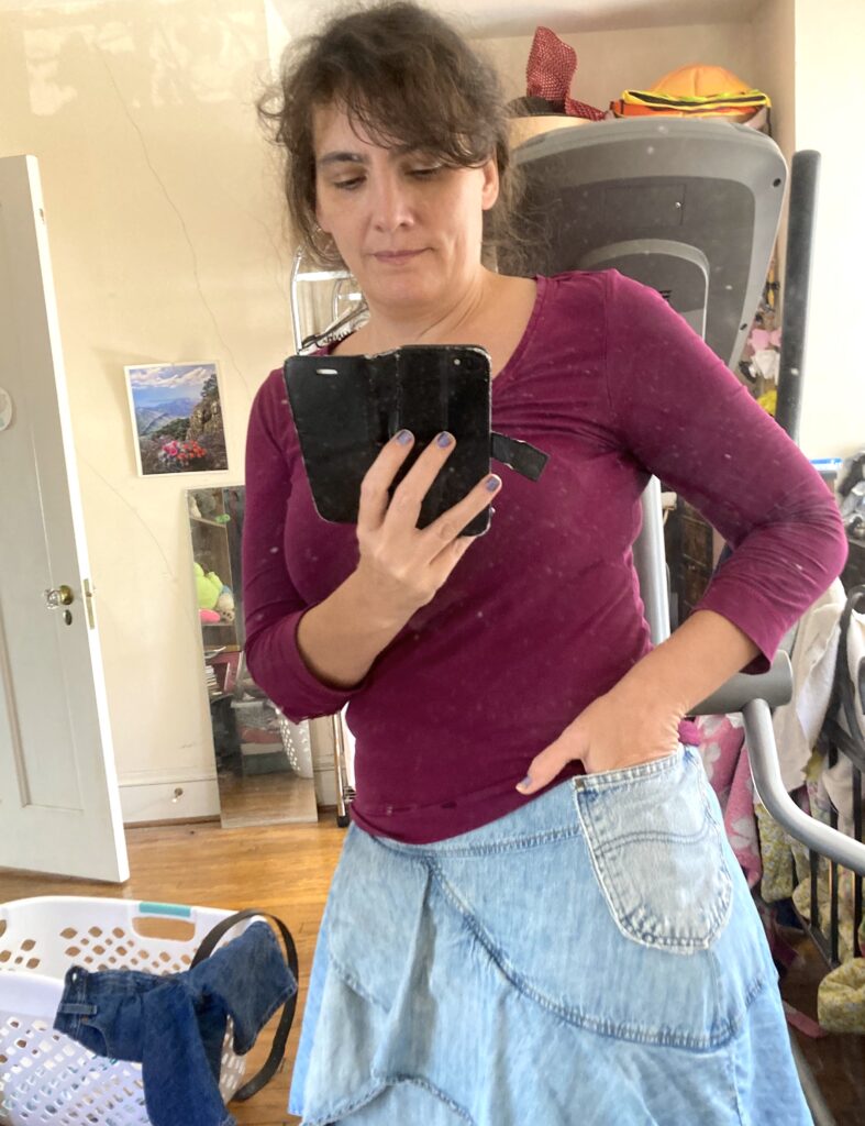 Mirror selfie with one hand in pocket of denim skirt